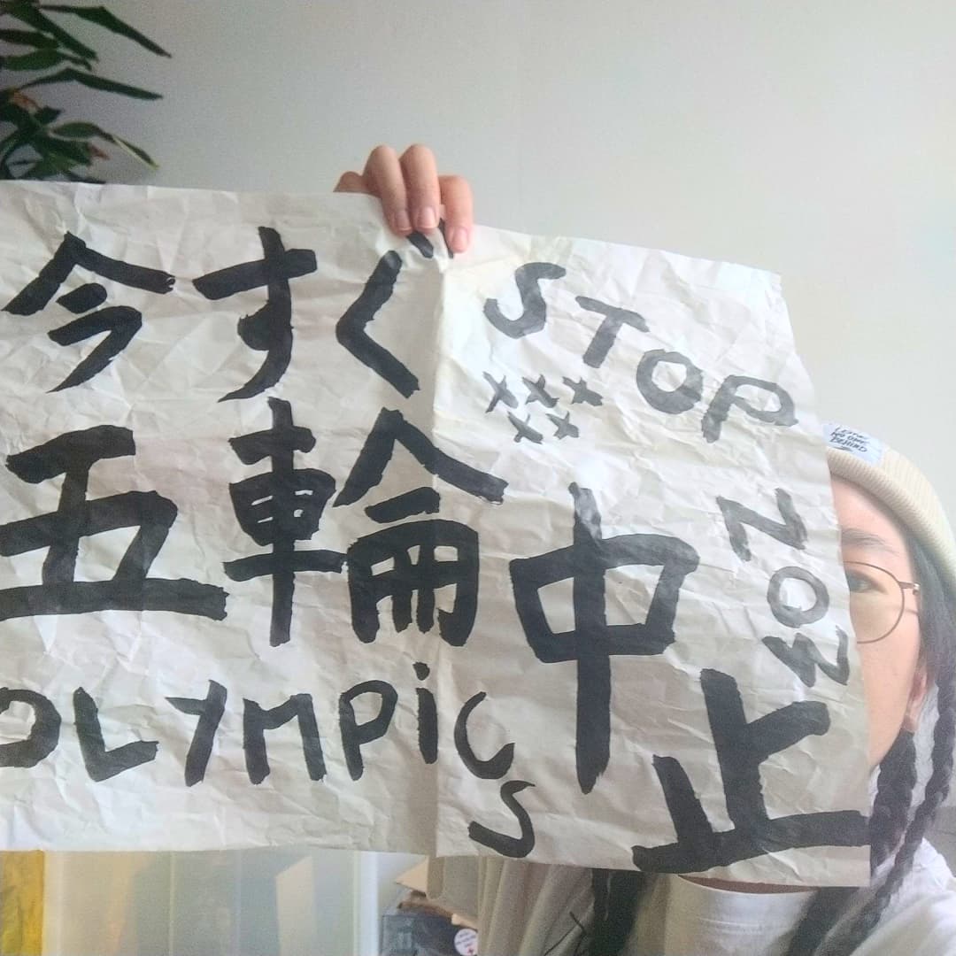 a person holding paper 今すぐ五輪中止　stop olympics now, looking from the side of the paper on the right corner