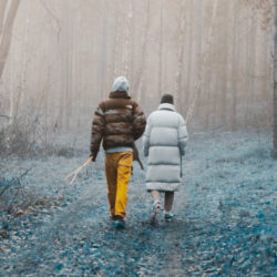 shot from behind of Ari (l) and Annett (r) walking in the Wood of Harz in winter. both in thick dawn coats. changed grey blue colour on the ground.