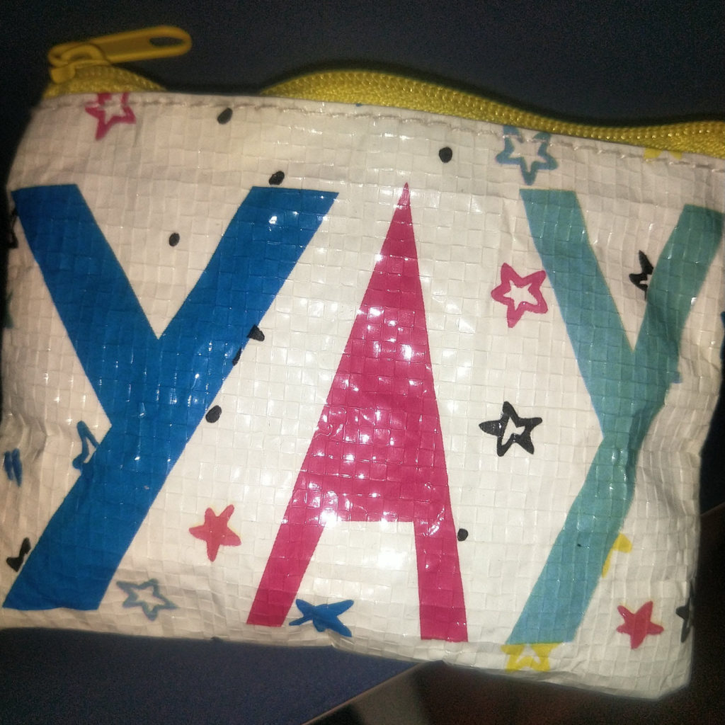 close up of a wallet. white plastic with yellow zipper, some stars in turqoise and magenta with big letter "YAY"