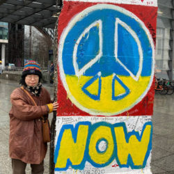 DJ Kohlrabi is standing next to the Wall of Berlin at Potsdamer Platz, Peace sign is painted in the Ukrainian colour